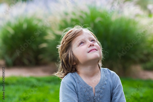 Young boy sitting on green lawn and looking up