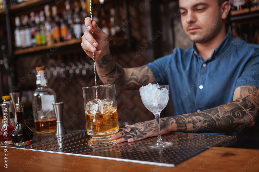 Cropped shot of a tattooed bartender working at his nightclub, mixing liquor, preparing cocktail