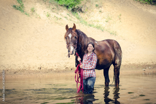 portrait of girl and red trakehner stallion horse in the river in the summer