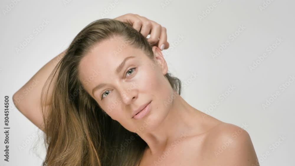 Close-up beauty portrait of young woman with smooth healthy skin, she gently touches hair with her hands and playfully looks at the camera on white background Close-up beauty portrait of young woman with smooth healthy skin, she gently touches hair with her hands and playfully looks at the camera on white background