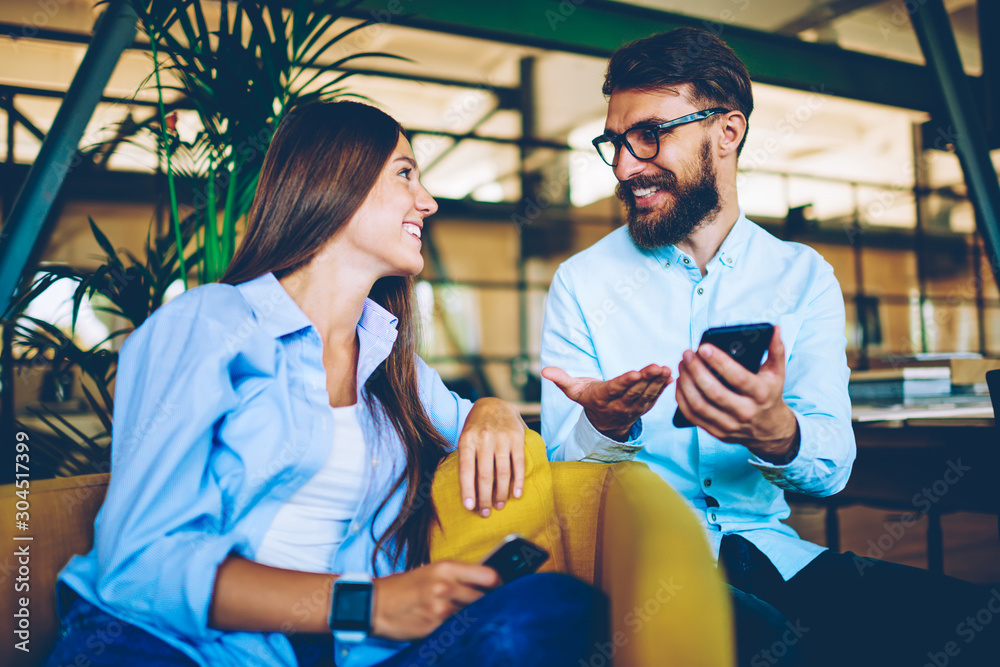 Obraz premium Male and female bloggers enjoying meeting together and communicating with followers in social networks via smartphone devices, two happy hipsters talking to each other in break of using gadgets