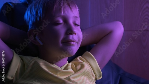 Boy listens to music in headphones. Cute boy lying on the couch and relaxing listening to music. Child rests in the evening in his room. Evening leisure of child 8 years.