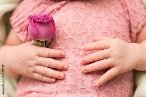 Happy Mother's day. hands of the newborn baby with pink rose flower