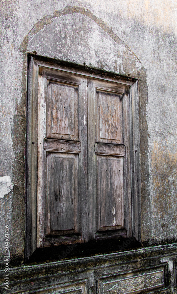 Old wooden window with Wood color shutters on weathered wall.