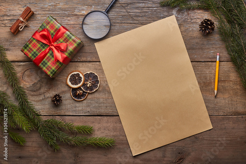 A wish list. Old paper sheet with pencil at grunge wooden background with copy space. Christmas tree, gift, cones, dried citrus fruits, magnifying glass, cinnamon