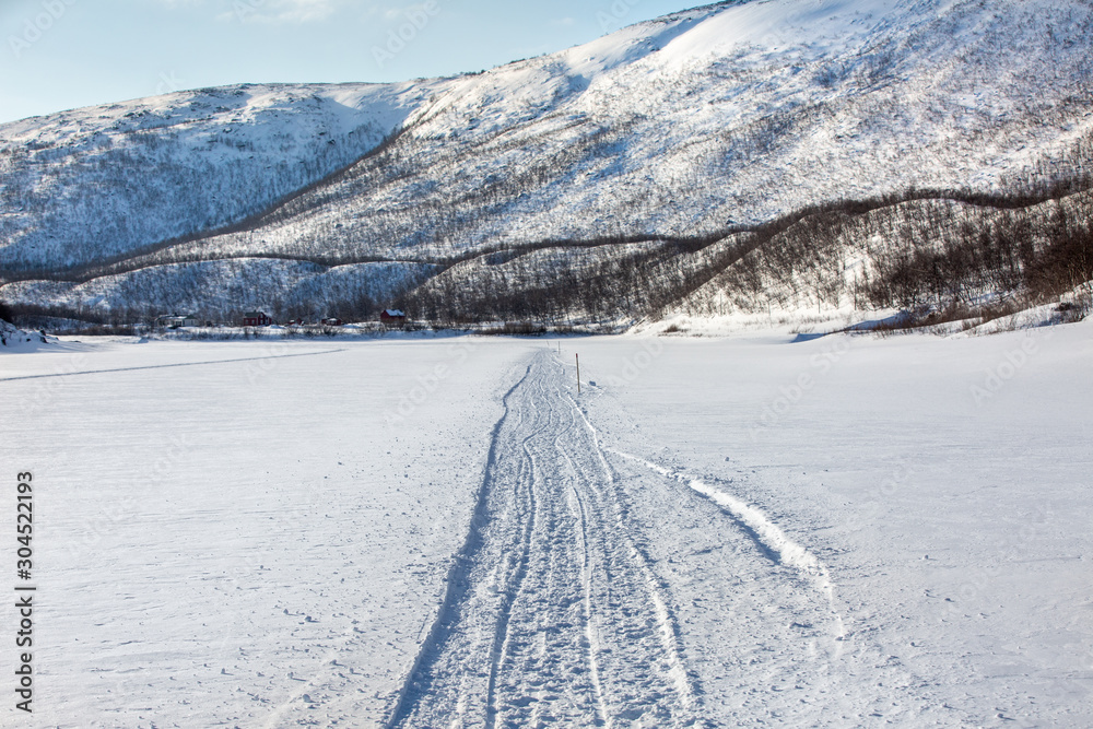 Snow mashin path on frozen riverbad to small village