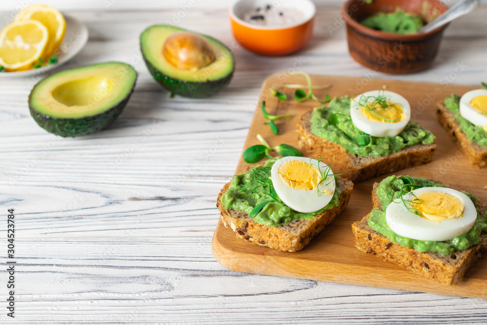 Healthy toasts with whole grain bread, avocado and boiled egg on wooden board.
