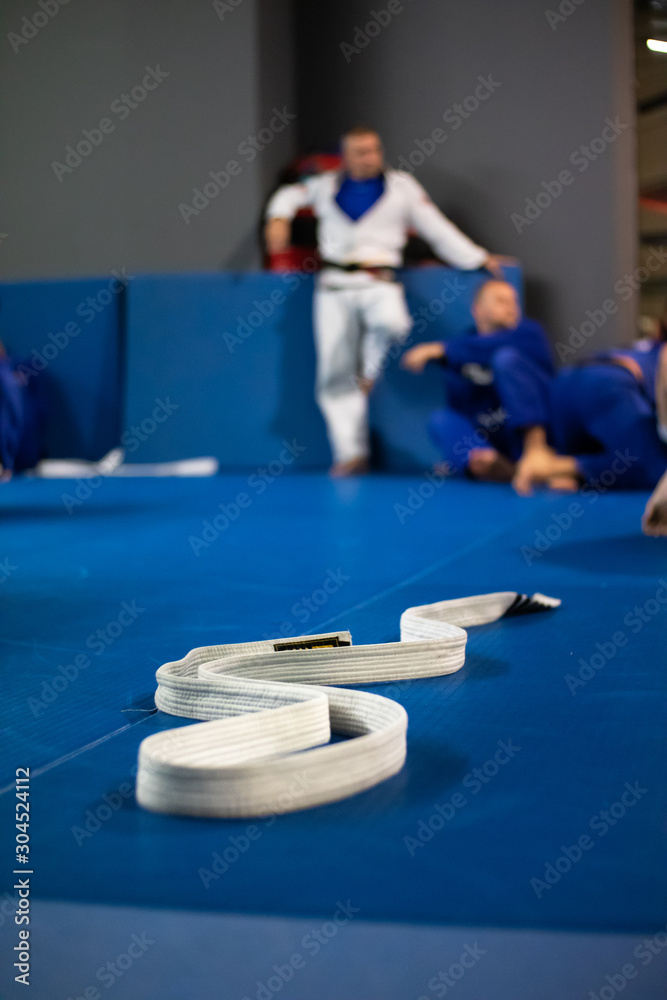 Brazilian jiu-jitsu training. White belt lying on the blue tatami. Jiu-jitsu  fighters in the background. Close-up, blurred background. Stock Photo |  Adobe Stock
