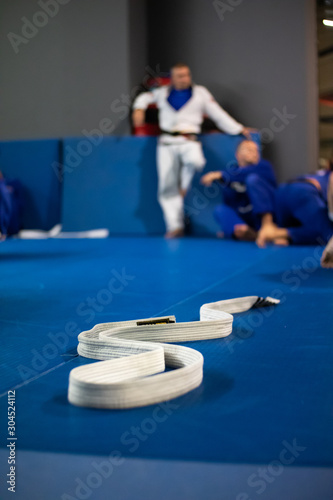 Brazilian jiu-jitsu training. White belt lying on the blue tatami. Jiu-jitsu fighters in the background. Close-up, blurred background. 