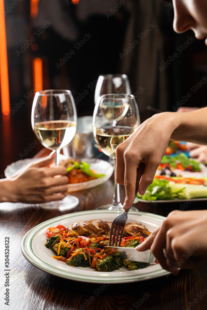 People having dinner in a restaurant with white wine and grilled chicken with vegetables on foreground