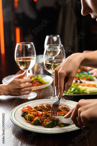 People having dinner in a restaurant with white wine and grilled chicken with vegetables on foreground photo