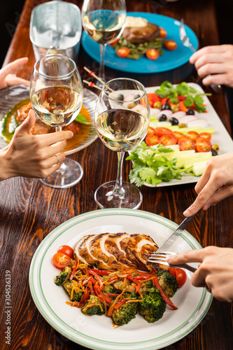People having dinner in a restaurant with white wine and grilled chicken with vegetables on foreground