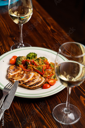 Grilled and sliced chicken breast with glasses of white wine on wooden table