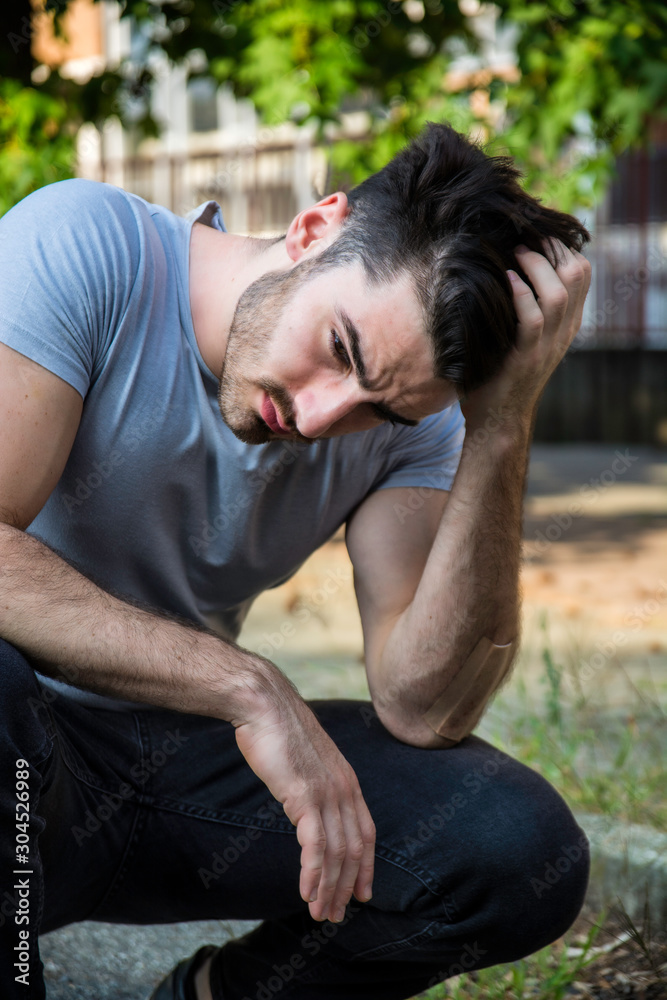 Depressed, sad young man scratching his head and looking up. Outoodr on the street Depressed, sad young man scratching his head and looking up. Outoodr on the street
