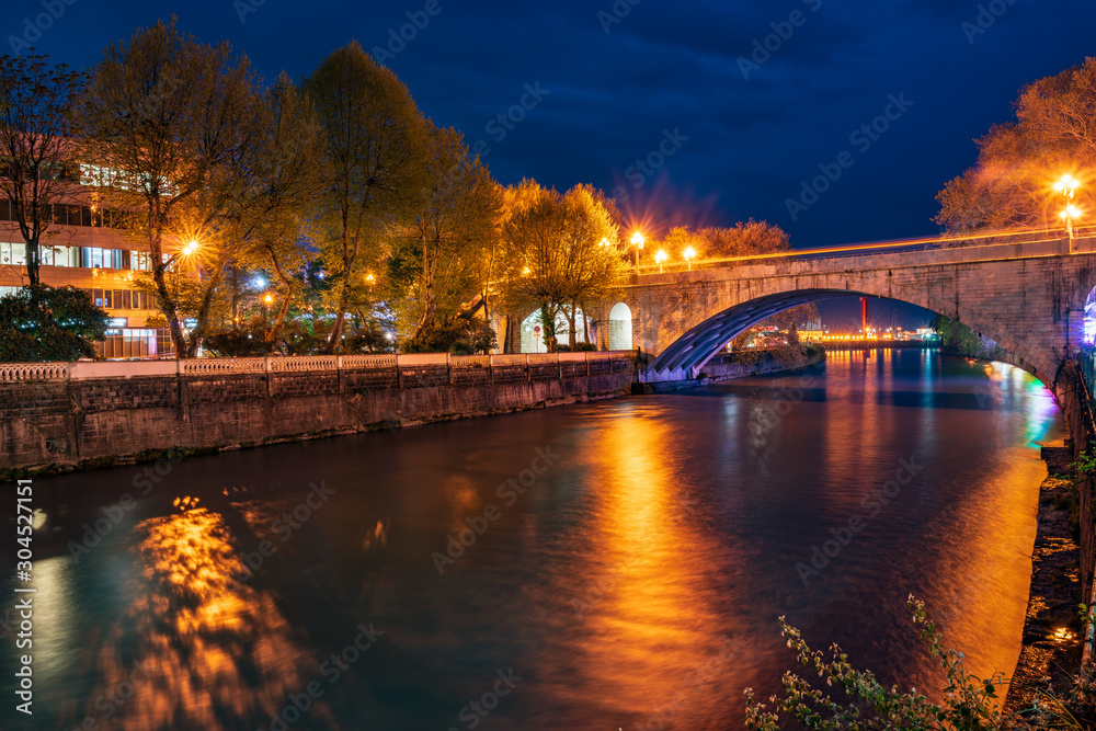 View of the stone bridge over the river at night with with rays of light and reflections