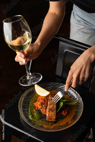 Woman is standing at the table with marinated chum salmon on it, holding a glass of white wine and fork