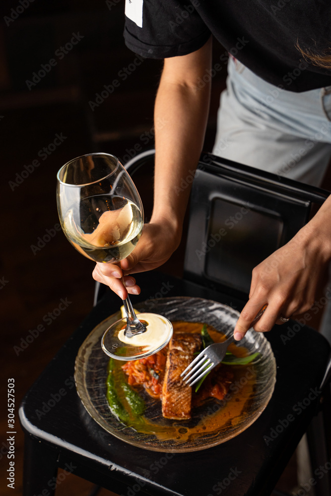 Woman is standing at the table with marinated chum salmon on it, holding a glass of white wine and fork Woman is standing at the table with marinated chum salmon on it, holding a glass of white wine and fork