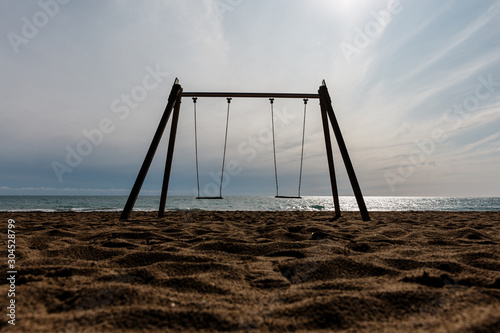 columpio sin nadie, parque infantil en la playa, sobre la arena en un día soleado. contraluz