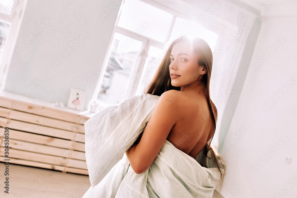 A beautiful long haired woman standing in white blanket in light room A beautiful long haired woman standing in white blanket in light room