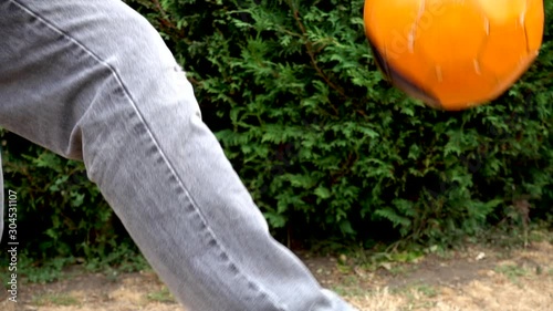 Close POV slow motion shot of an adult man’s leg using a small orange football for keepy-uppy repetitions in a garden / yard. photo