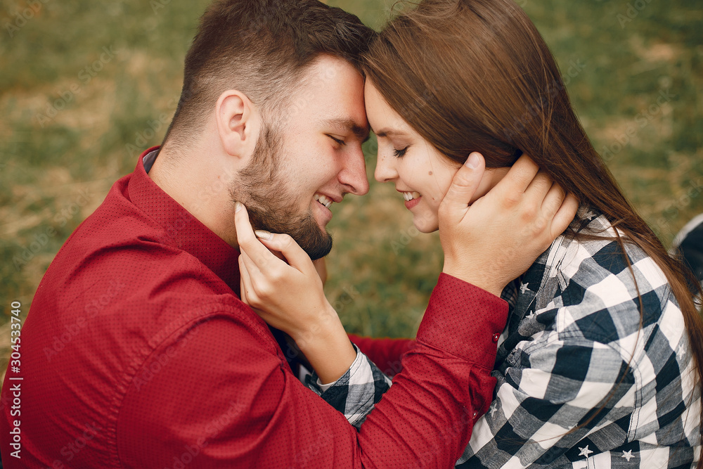 Fototapeta premium Cute couple in a park. Lady in a chirt. Guy in a red shirt
