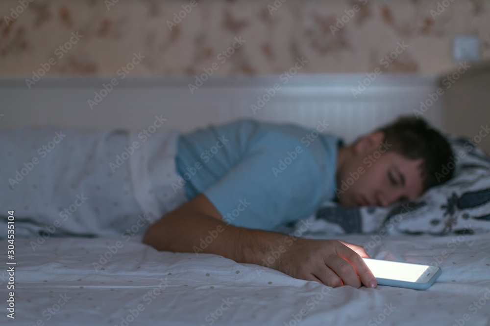 Man fell asleep with smartphone in the hand. Male uses the cell phone too much and suffers from sleep disorders. Social media and internet addiction. Health care concept. Selective focus on telephone. Man fell asleep with smartphone in the hand. Male uses the cell phone too much and suffers from sleep disorders. Social media and internet addiction. Health care concept. Selective focus on telephone.