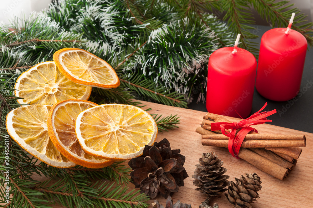 Christmas composition - candle, cones, dried orange, cinnamon, fir tree branch. On wooden background.