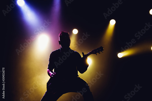 Guitarist plays solo. silhouette of guitar player in action on music stage. popular music rock band performs on stage.