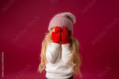 little blonde girl in a knitted hat and mittens smiles. winter clothes