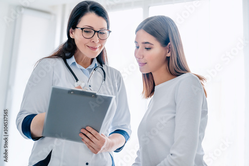 Fotografia Smiling adult female doctor reporting medical results to young girl patient