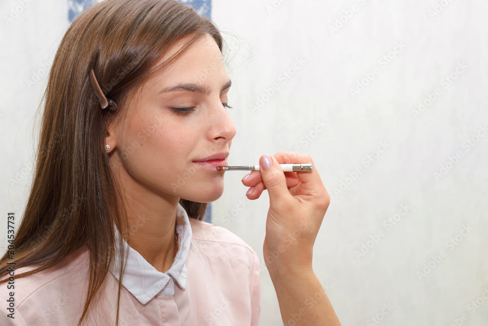 Makeup artist applies gloss on lips of model. Makeup artist applies gloss on lips of model.