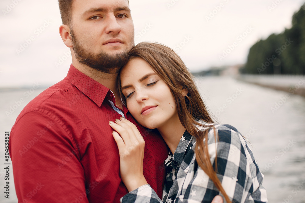 Cute couple in a park near river. Lady in a chirt. Guy in a red shirt Cute couple in a park near river. Lady in a chirt. Guy in a red shirt