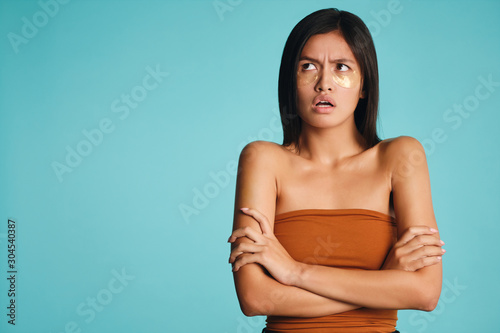 Upset Asian girl with patches under eyes holding hands crossed offendedly looking away over colorful background isolated © Anton