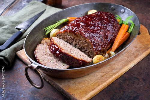 Traditional American meatloaf with ketchup from ground beef with carrots and onion as closeup in a copper saucepan
