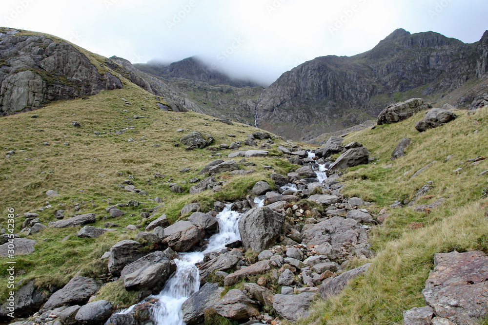 Mountain stream leads up towards Clogwyn with Snowdon shrouded in cloud, Snowdonia National Park, North Wales