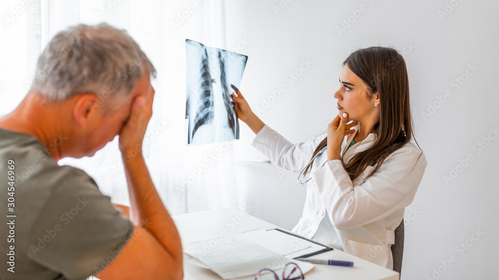 Fototapeta premium Doctor showing X-ray to patient, elder men felt worried about result from a female doctor. Shot of a female doctor watching X-rays with her senior worried patient