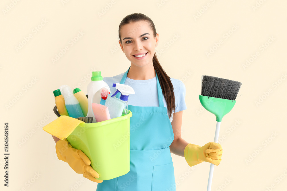 Female janitor with cleaning supplies on light background Female janitor with cleaning supplies on light background