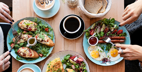 Healthy breakfast on a plate with coffee cup during the meeting  in restaurant. Hands of women with cutlery. Colorful food. Close up and flat lay.