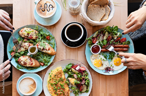 Different colorful meals for breakfast or lunch time on a plate with cutlery on woman's hands. Fried eggs, omelette, bruschetta and sausage on a wooden teble in restaurant. Flat lay top view. photo