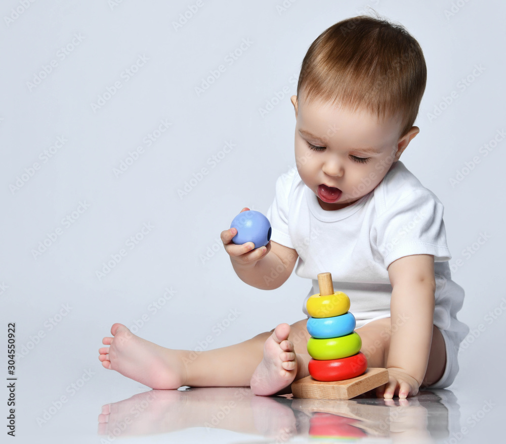 Newborn baby boy toddler playing and playing with a childrens multi-colored developing pyramid on a gray Newborn baby boy toddler playing and playing with a childrens multi-colored developing pyramid on a gray