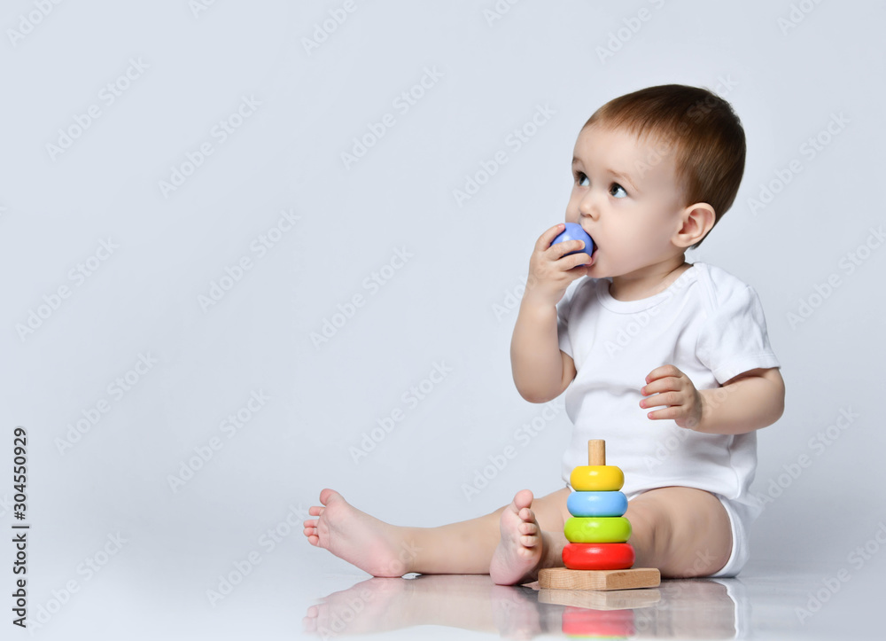 Newborn baby boy toddler playing and playing with a childrens multi-colored developing pyramid on a gray Newborn baby boy toddler playing and playing with a childrens multi-colored developing pyramid on a gray