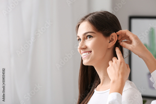 Woman putting hearing aid in young girl's ear at home photo