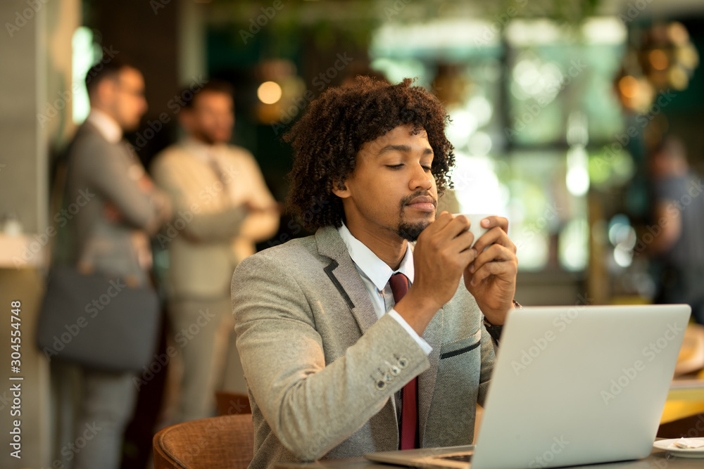 Young afro american business siting in a pub and drinking morning coffee