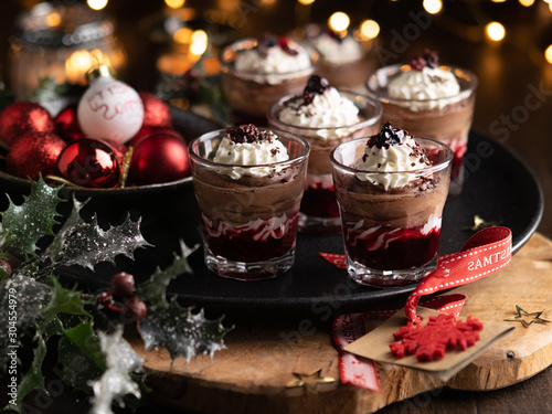 Dessert in a glasses with chocolate and berries spread on wooden background with garland lights bokeh and christmas decoration. New year holidays background concept. Dessert recipe ideas.