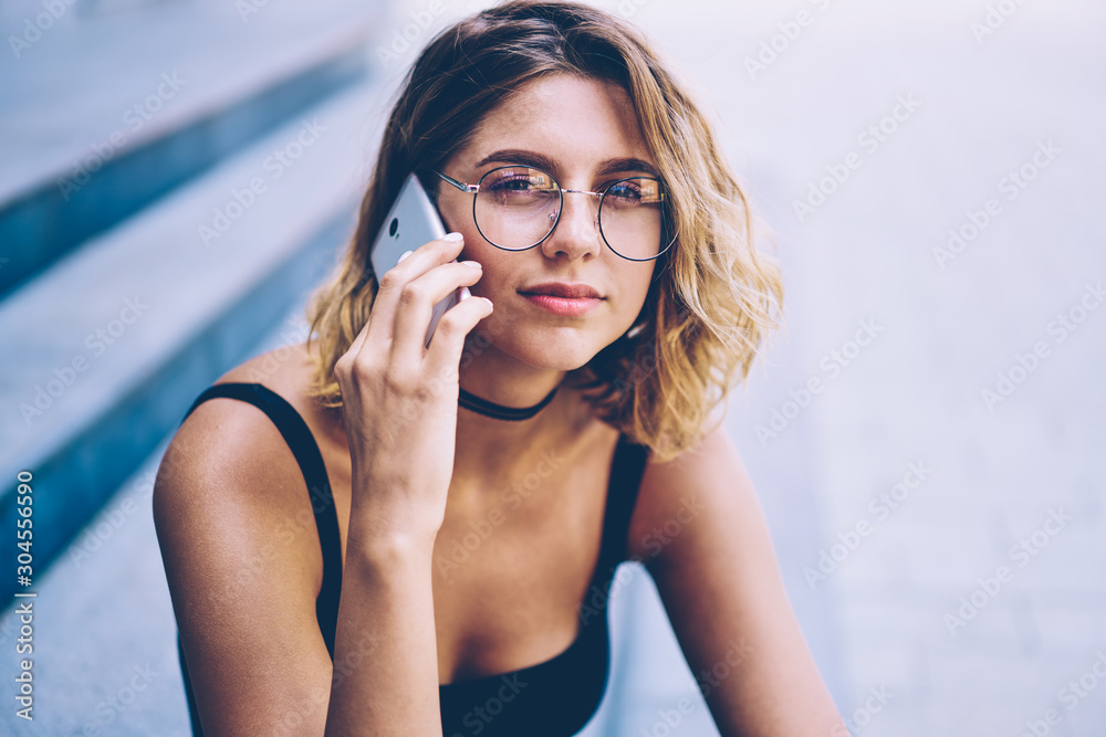 Close up portrait of attractive hipster girl in trendy sunglasses looking at camera during international smartphone conversation, charming woman calling to operator during free time outdoors Close up portrait of attractive hipster girl in trendy sunglasses looking at camera during international smartphone conversation, charming woman calling to operator during free time outdoors