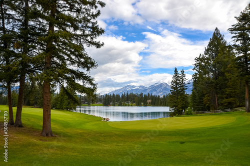 The perfectly cut, vibrant green grass of the Whistler golf course and it’s tall pine trees creates a beautiful foreground to the calm waters edge of the lake and mountains in the distance on this par