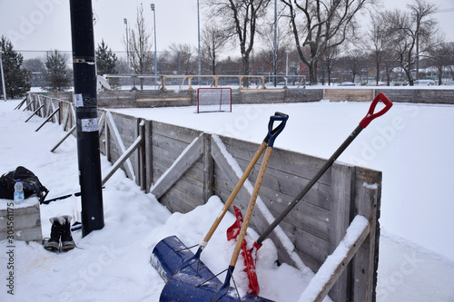 Large snow shovels leaning on a Canadian hockey ice rink outdoors during snow fall, Montreal, Canada