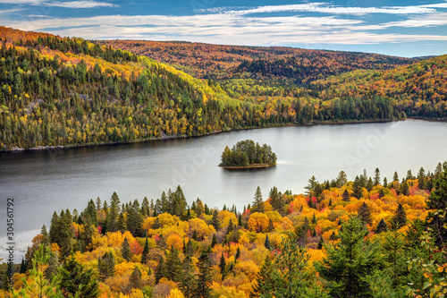 Pine Island in the middle of Wapizagonke lake surrounded by colorful forested hills in Autumn, La Mauricie National Park, Quebec, Canada