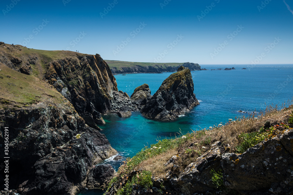 A picturesque landscape of Kynance Cove in Cornwall with rugged cliffs over looking a clear blue ocean in summer sunshine