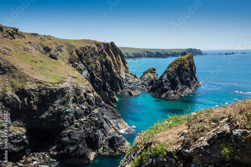 A picturesque landscape of Kynance Cove in Cornwall with rugged cliffs over looking a clear blue ocean in summer sunshine